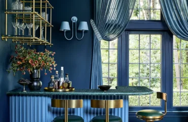 Bold blue bar room with deep navy walls, fluted blue cabinetry, brass detailing, and green leather stools, designed by Andrew Suvalsky Designs in Great Falls, Virginia